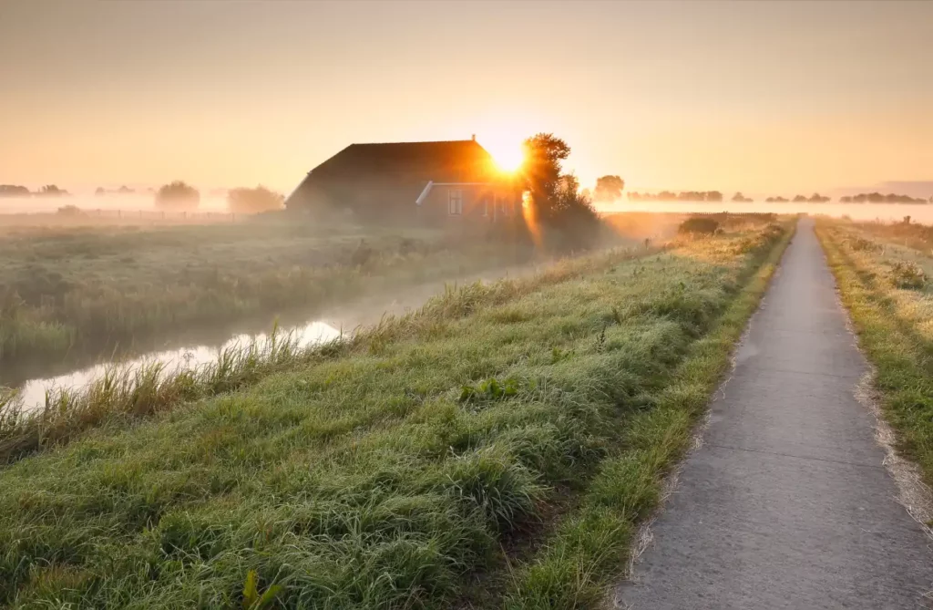 Radweg am Bauernhaus bei nebligem Sonnenaufgang